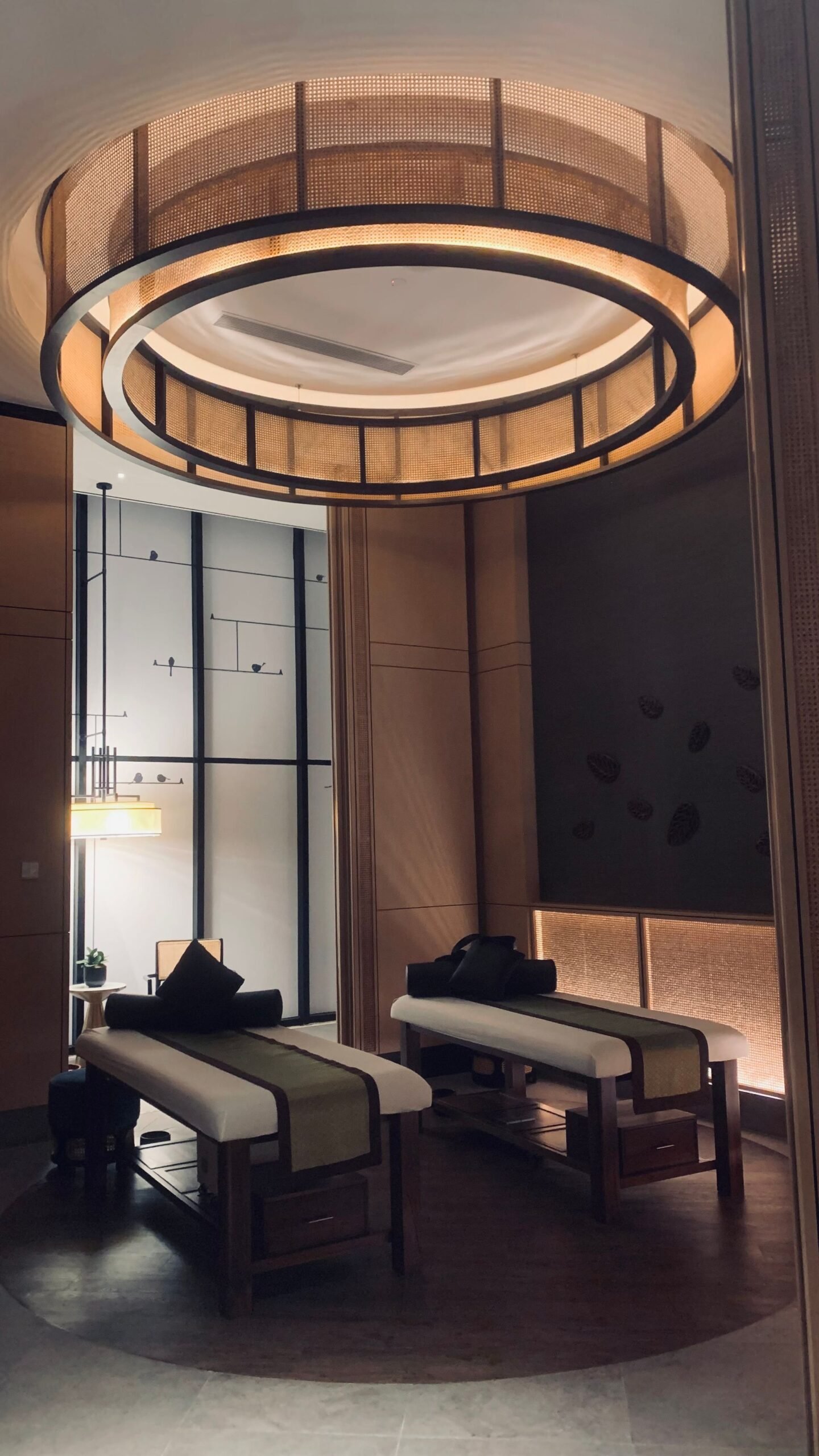 Warm, softly lit spa interior with a circular wood-slat light fixture above treatment beds