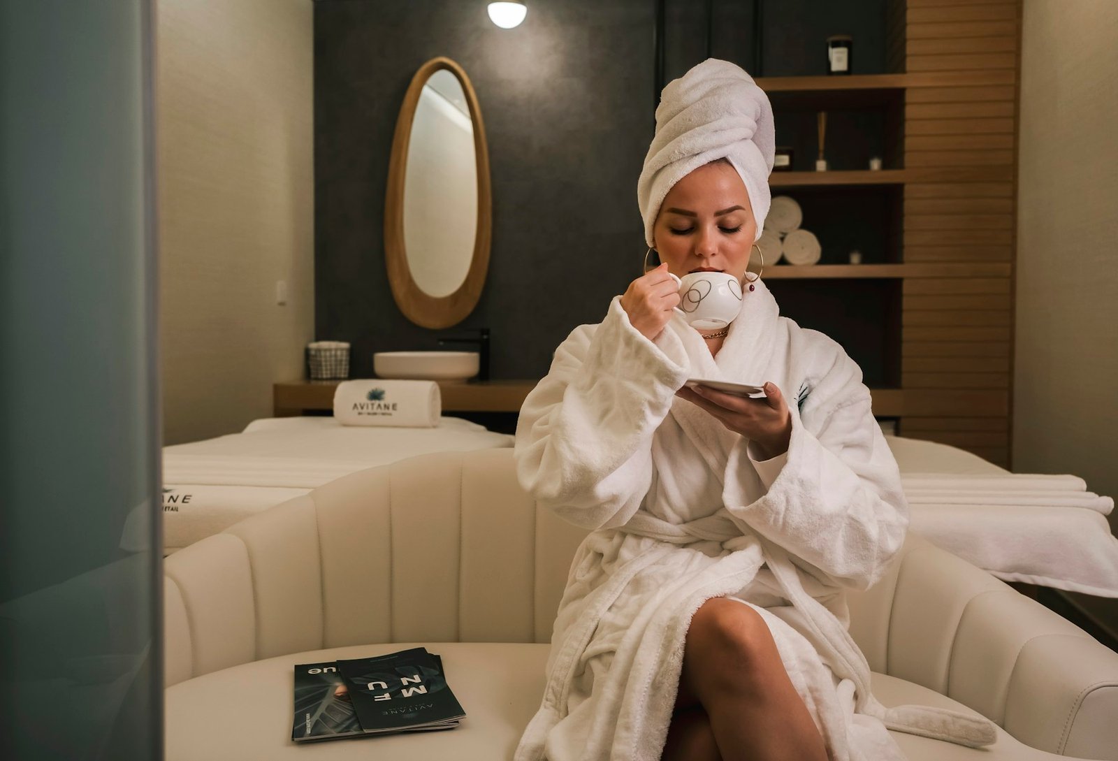 Guest in a robe pausing with tea in a warm spa lounge