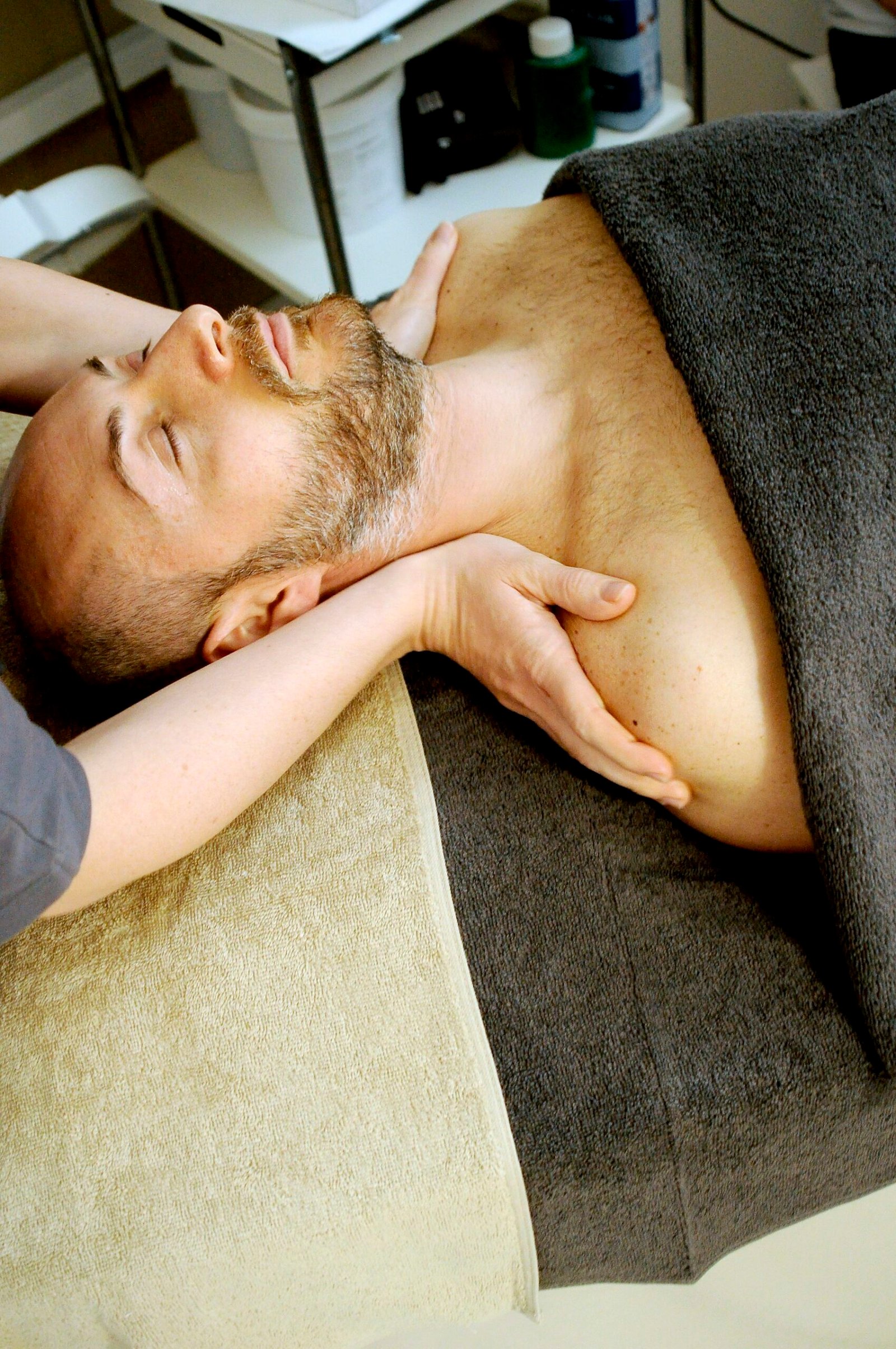Bearded man lying calmly, receiving a neck and shoulder massage