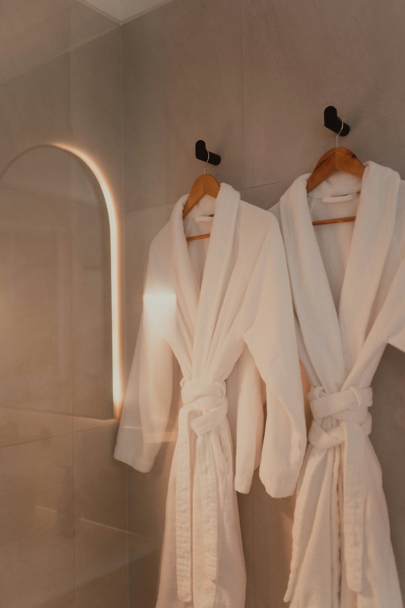 Two white bathrobes hanging on hooks in a modern warm-toned bathroom