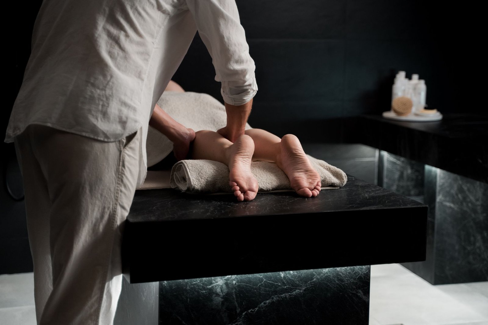 Therapist performing a premium foot and leg massage in a dark marble treatment room